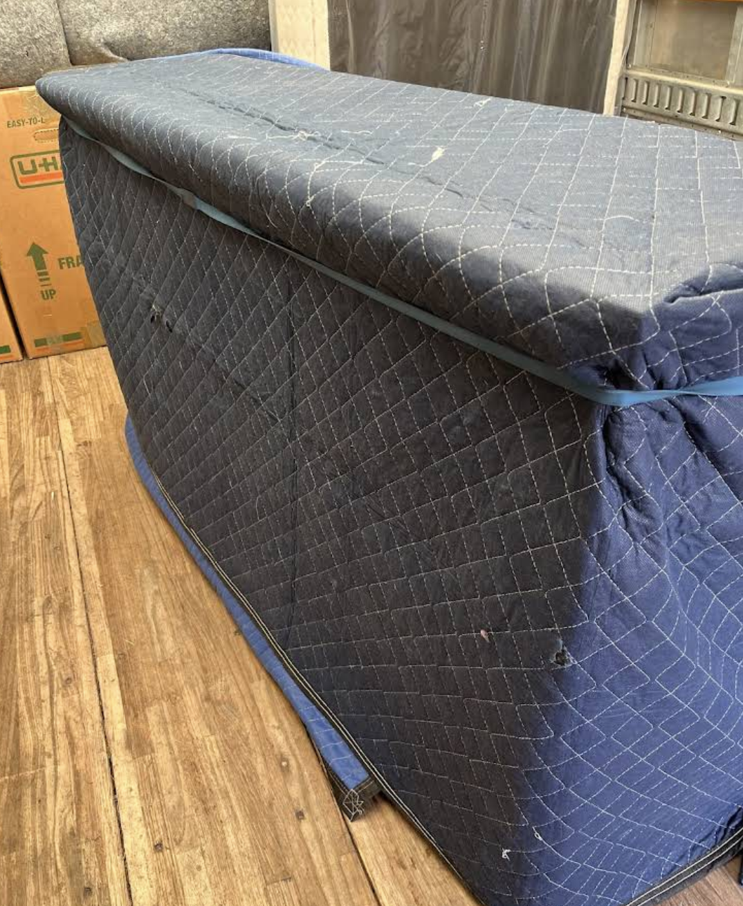 A furniture piece fully wrapped in moving blankets for protection during transport