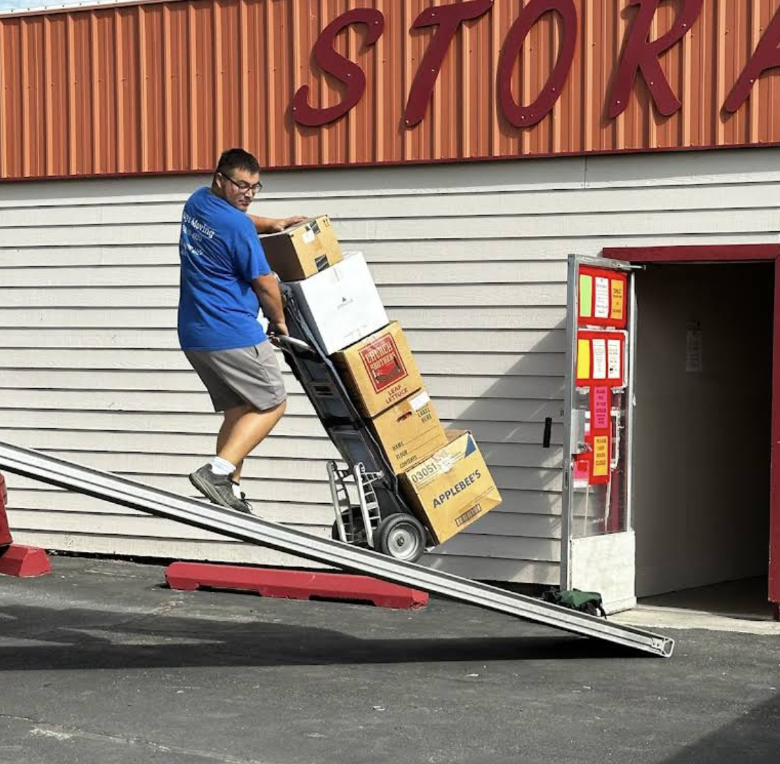 A Chuy's Moving worker guiding boxes into a storage unit using a ramp